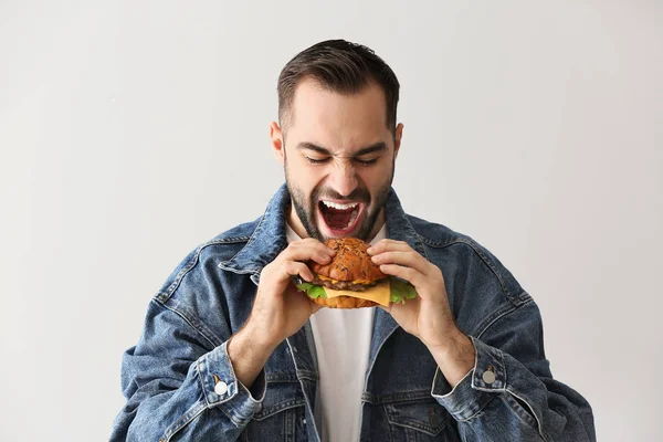 Man eating tasty burger on light background — Stock Photo, Image