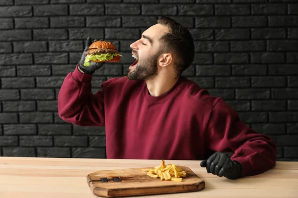 Homme mangeant hamburger savoureux avec des frites à table — Photo