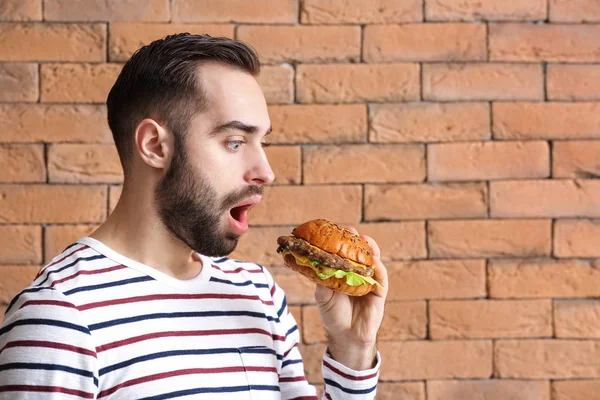 Uomo sorpreso con gustoso hamburger contro muro di mattoni — Foto Stock