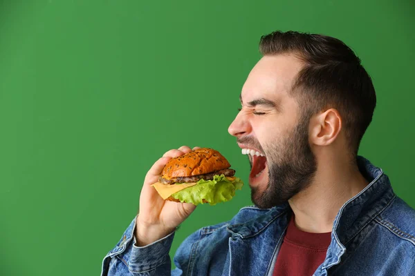 Mann isst leckeren Burger auf farbigem Hintergrund — Stockfoto