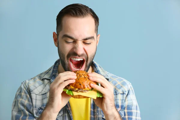 Человек ест вкусный бургер на цветном фоне — стоковое фото
