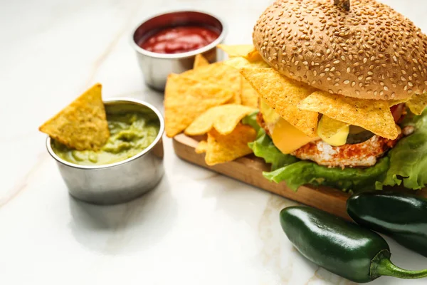 Tasty burger with nachos, tomato sauce and guacamole on table — Stock Photo, Image