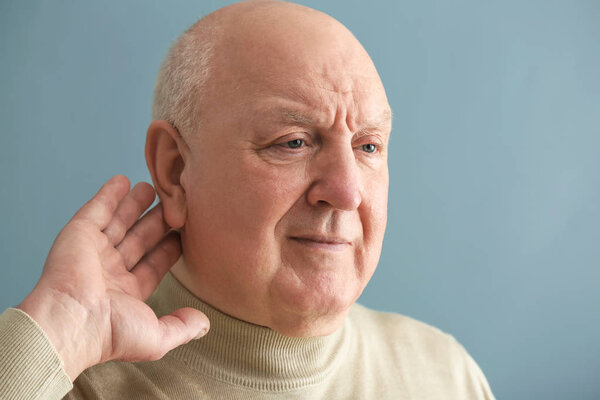 Старший мужчина с проблемами со слухом на фоне цвета
