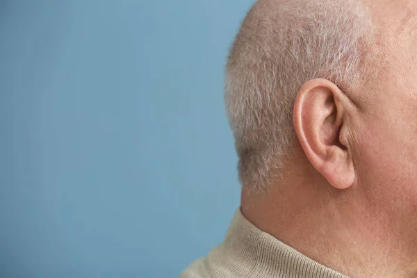 Senior man met hoorzitting probleem op kleur achtergrond, close-up — Stockfoto