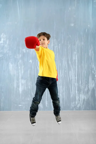 Χαριτωμένο μικρό αγόρι σε γάντια του μποξ άλματα τοίχο γκρι — Φωτογραφία Αρχείου