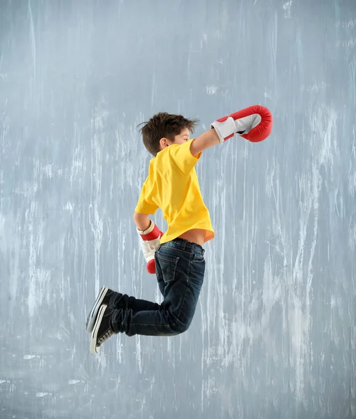 Χαριτωμένο μικρό αγόρι σε γάντια του μποξ άλματα τοίχο γκρι — Φωτογραφία Αρχείου