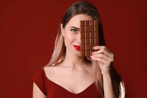 Schöne junge Frau mit leckerer Schokolade auf farbigem Hintergrund — Stockfoto