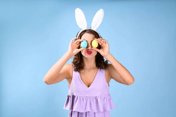 Mooie jonge vrouw met bunny oren en paaseieren op kleur achtergrond — Stockfoto