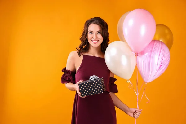 Beautiful young woman with gift and balloons on color background — Stock Photo, Image