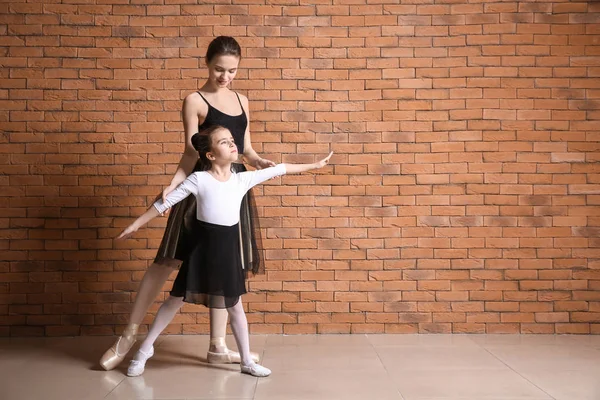 Pequena bailarina com treinador contra parede de tijolo — Fotografia de Stock