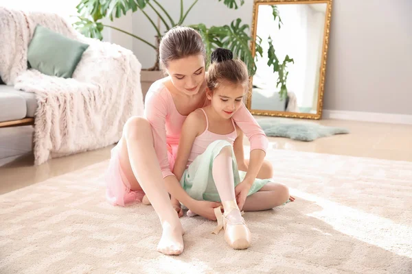 Coach helping little ballerina to put on point shoes at home