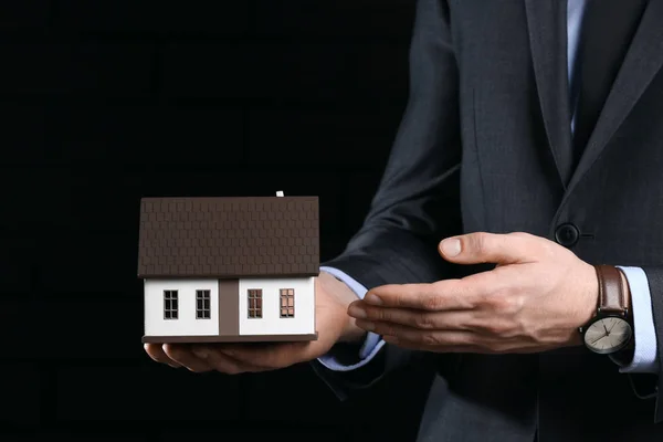 Agente de seguros con modelo de casa sobre fondo oscuro, primer plano. Protección de la casa contra el terremoto — Foto de Stock