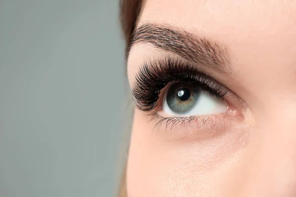 Young woman with beautiful eyelashes on grey background, closeup — Stock Photo, Image