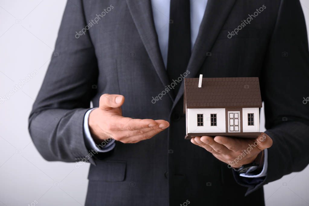 Insurance agent with model of house on light background, closeup. Protection of house from earthquake