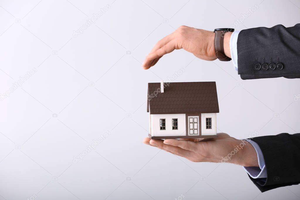 Insurance agent with model of house on light background. Protection of house from earthquake