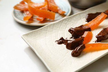 Tasty chocolate covered orange peels on plate, closeup clipart