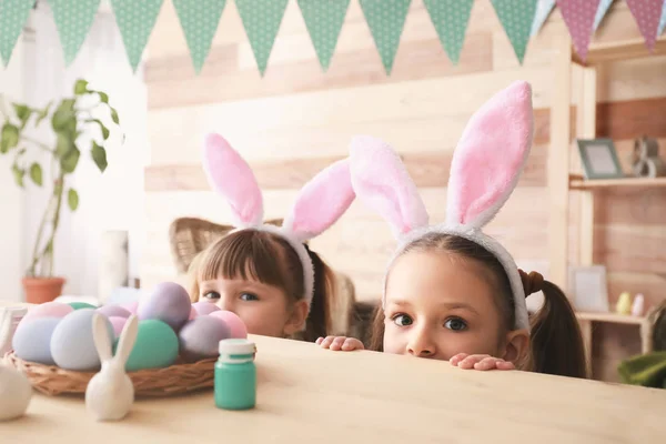 Симпатичні маленькі дівчата ховаються за столом з великодніми яйцями — стокове фото