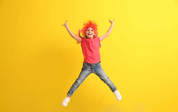 Funny little girl in wig jumping against color background — Stock Photo, Image