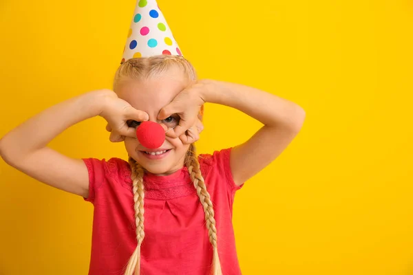 Niña divertida con nariz de payaso y sombrero de fiesta sobre fondo de color. Celebración del Día de los Inocentes — Foto de Stock