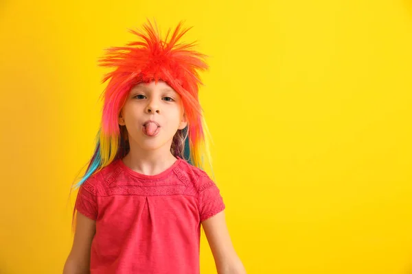 Funny little girl in wig showing tongue on color background. April fools' day celebration — Stock Photo, Image