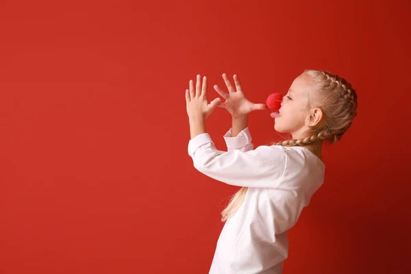 Funny little girl with clown nose on color background. April fools' day celebration — Stock Photo, Image