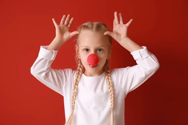 Funny little girl with clown nose on color background. April fools' day celebration — Stock Photo, Image