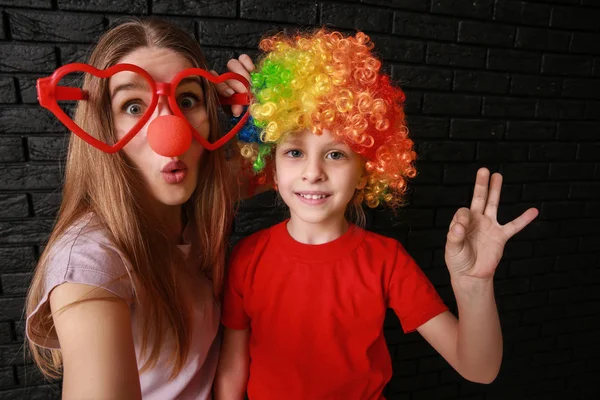 Woman and little girl in funny disguise on dark background. April fools' day celebration — Stock Photo, Image