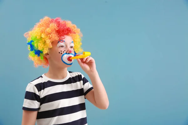 Lindo niño con maquillaje de payaso y silbato de fiesta en el fondo de color. Celebración del Día de los Inocentes — Foto de Stock