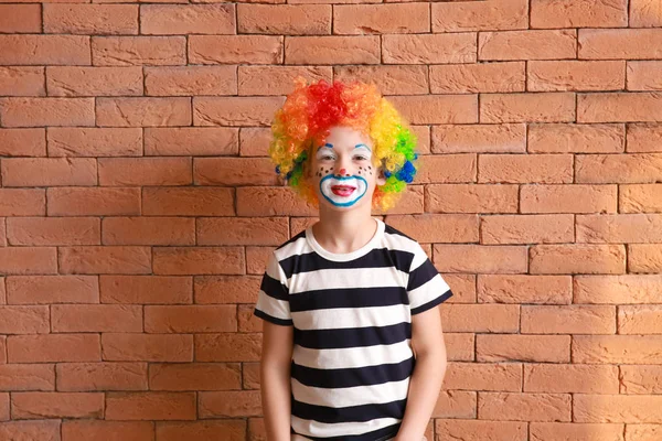Netter kleiner Junge mit Clown-Make-up gegen Ziegelwand. Aprilscherz-Fest — Stockfoto