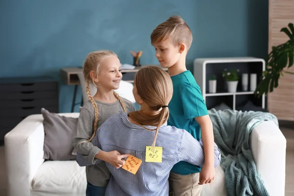 Children attaching paper sheets with text KICK ME and APRIL FOOLS' DAY to their mother's back — Stock Photo, Image