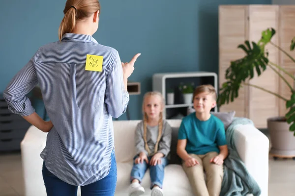 Woman scolding children who attached paper sheets with text KICK ME to her back. April fools' day prank — Stock Photo, Image