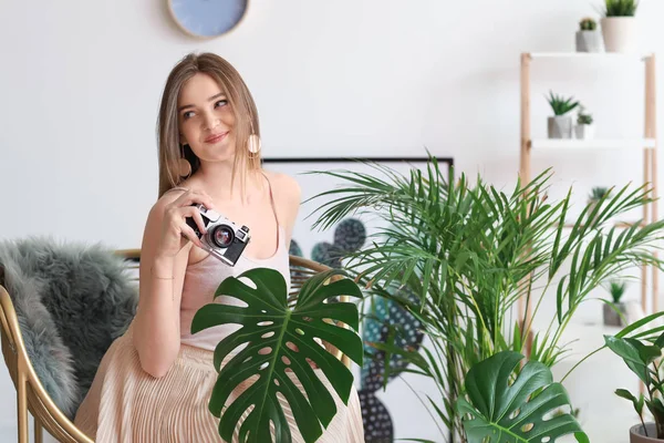 Portrait of beautiful woman with green tropical plants and photo camera indoors — Stock Photo, Image