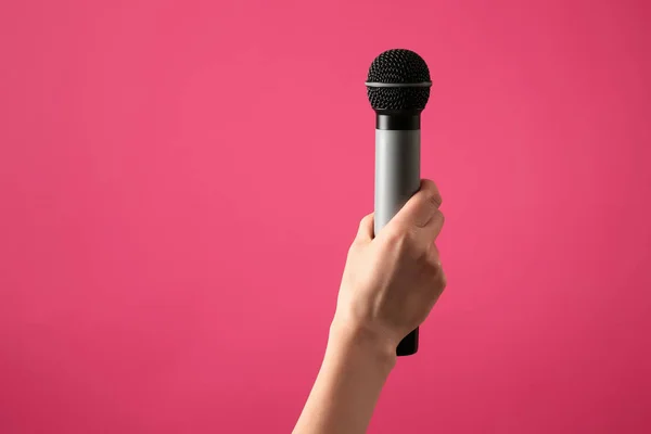 Mano femminile con microfono su sfondo a colori — Foto Stock