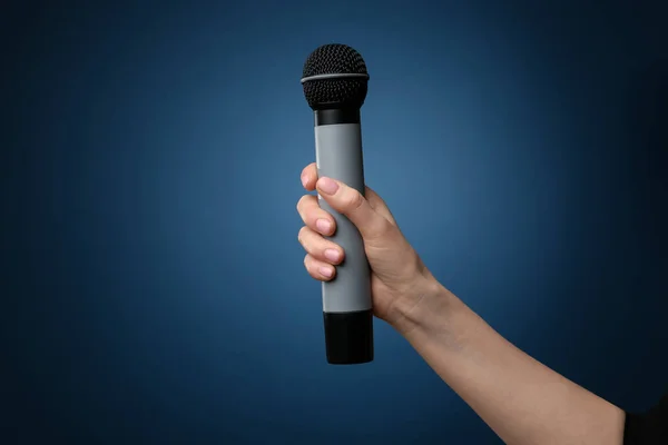 Mano femenina con micrófono sobre fondo de color — Foto de Stock