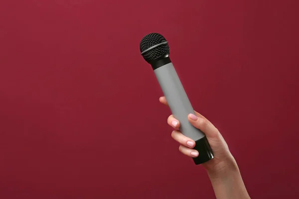 Mano femenina con micrófono sobre fondo de color — Foto de Stock