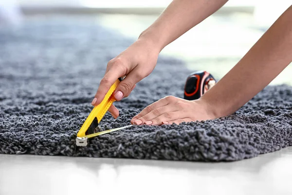 Woman with tape measure cutting carpet on floor — Stock Photo, Image