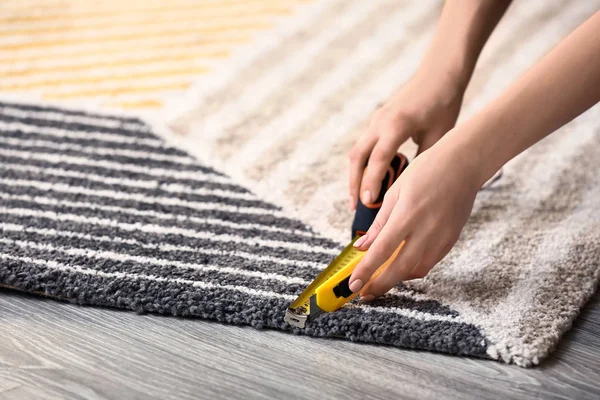 Woman with tape measure cutting carpet on floor — Stock Photo, Image