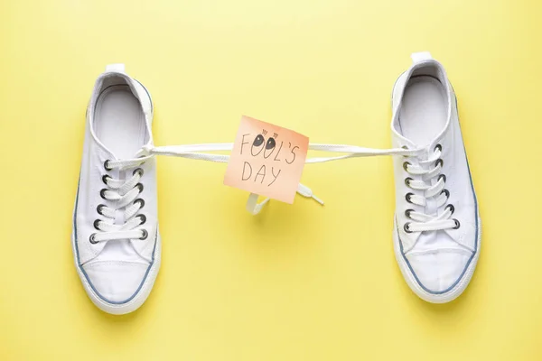 Shoes with tied together laces and sticky note with text FOOL\'S DAY on color background