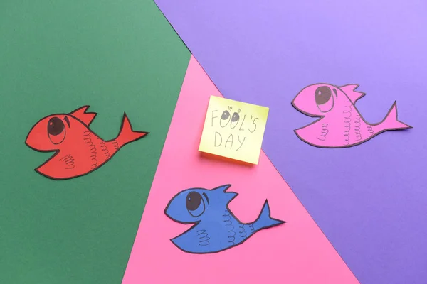 Peces de papel y nota adhesiva con texto DÍA DEL Tonto sobre fondo de color — Foto de Stock