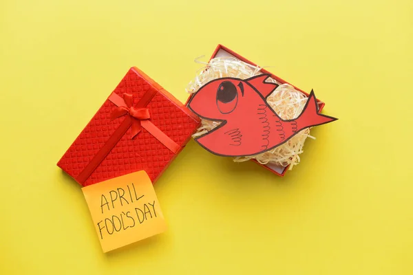 Box with paper fish and sticky note with text APRIL FOOL'S DAY on color background — Stock Photo, Image