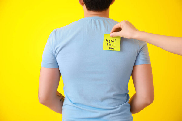 Женщина приклеивает бумагу к спине своей подруги на цветном фоне. Шутка в честь Дня дураков
