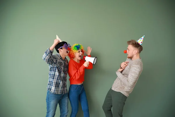 Funny people with megaphone shouting at their friend against color background. April Fools' Day prank — Stock Photo, Image