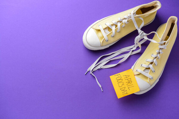 Shoes with tied together laces and sticky note with text APRIL FOOL'S DAY on color background Stock Picture