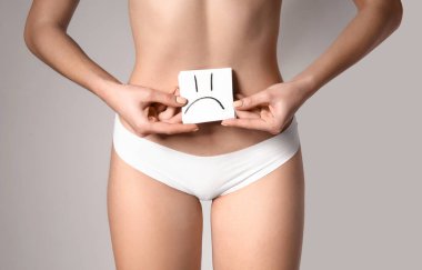 Güzel genç kadın gri arka planda çizilmiş duygu ile kağıt tutarak. Sağlık konsepti