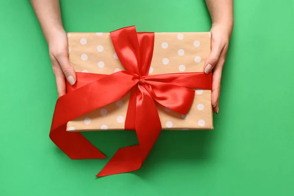 Руки женщины с подарочной коробкой на цветном фоне — стоковое фото
