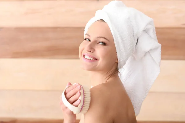 Mulher bonita com escova de massagem em fundo de madeira — Fotografia de Stock