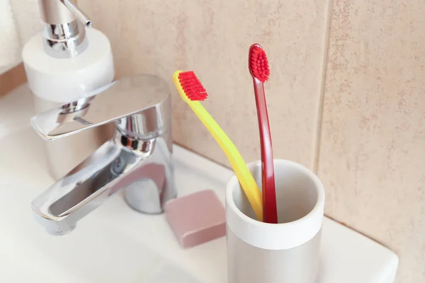 Holder with toothbrushes on sink in bathroom