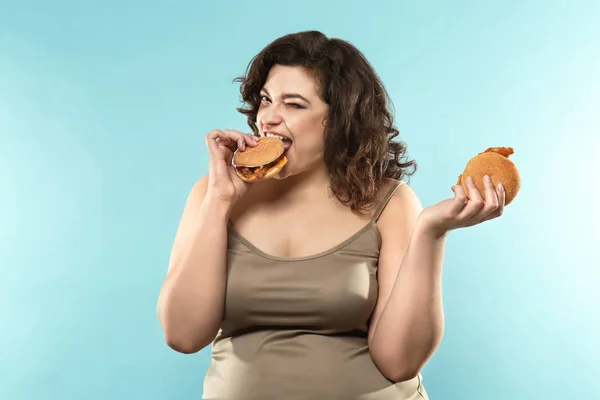 Overweight woman with burgers on color background — Stock Photo, Image