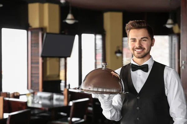 Young male waiter with tray and cloche in restaurant — Stock Photo, Image