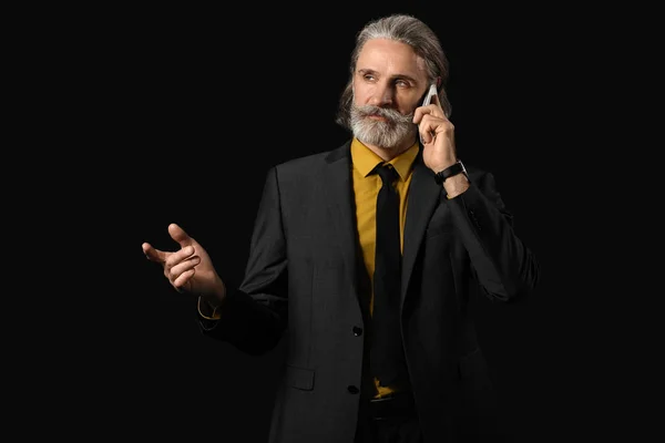 Handsome mature businessman talking by phone on dark background — Stock Photo, Image